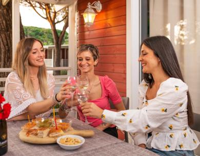 Tre amiche brindano insieme all'aperto, con cibo e vino.