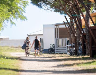 Coppia cammina su un sentiero alberato vicino a case e biciclette.