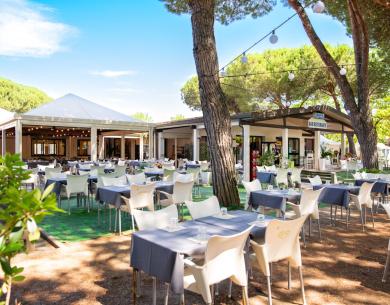 Ristorante all'aperto con tavoli apparecchiati sotto gli alberi.