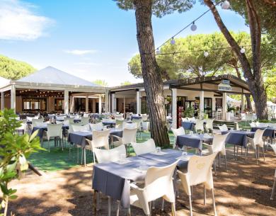 Restaurant en plein air avec tables sous les arbres, ambiance chaleureuse.