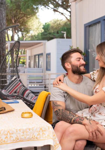 Lächelndes Paar umarmt sich auf einer Veranda mit Blumen und Brettspielen.