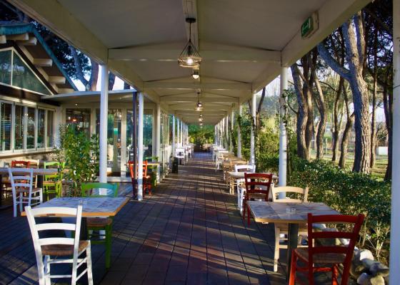 Ristorante all'aperto con sedie colorate e alberi intorno.