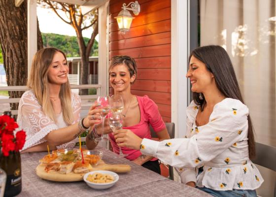 Tre amiche brindano insieme all'aperto, con cibo e vino.