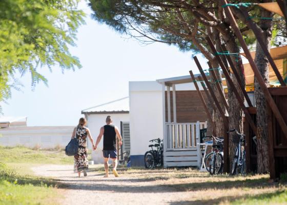 Coppia cammina su un sentiero alberato vicino a case e biciclette.