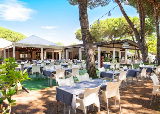 Ristorante all'aperto con tavoli apparecchiati sotto gli alberi.